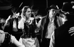 fot. Dorota Awiorko / [Trzymająca się pod ramiona grupa młodych, uśmiechniętych ludzi w strojach ludowych. Za nimi dwóch skrzypków.]