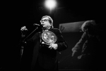 fot. Dorota Awiorko / [Mężczyzna w okularach, przy mikrofonie na statywie, trzymający statuetkę w kształcie gongu. Tło ciemne.]