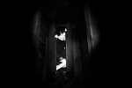 fot. Dorota Awiorko / [Kobieta leżąca w czarnej skrzyni, podtrzymująca rękami półprzymknięte drzwiczki. Dookoła ciemność.]