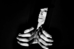 fot. Dorota Awiorko / [Zbliżenie na dłonie wyłaniające się z niewielkiej szpary w pozycji jakby chciały ją jeszcze bardziej rozchylić, za utworzoną w czarnej kotarze przerwą fragment twarzy kobiety.]