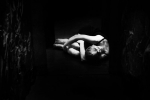 fot. Dorota Awiorko / [Ujęcie z góry. Kobieta siedząca na ziemi i oplatająca rękami podciągnięte do siebie kolana, wspierająca opuszczoną głowę na ręce. Tło czarne.]