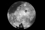 Zdjęcie czarno-białe. Księżyc w pełni na dużym okrągłym ekranie. W dolnej części ujęty popiersiowo mężczyzna. Tło czarne. / fot. W.Nieśpiałowski