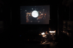 fot. Wojciech Nieśpiałowski / [Po prawej stronie sceny muzyk przy fortepianie. Nad sceną ekran z wyświetlonym nocnym widokiem miasta, z nałożonym na ten obraz wielkim księżycem w pełni.]